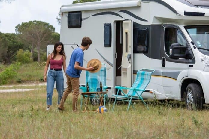 A young couple setting up chairs and a table outside their RV in a grassy field