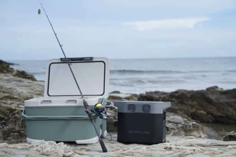 EcoFlow portable power station next to an open cooler and fishing rod on a rocky shoreline