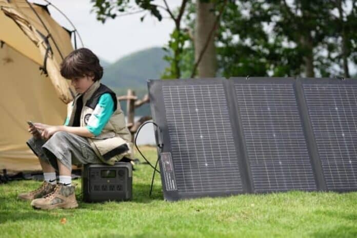 The boy sits next to a portable power station and foldable solar panels