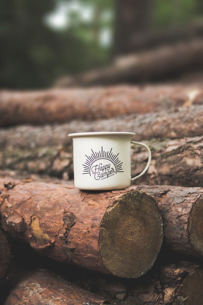 white happy camper printed cup on brown wooden log